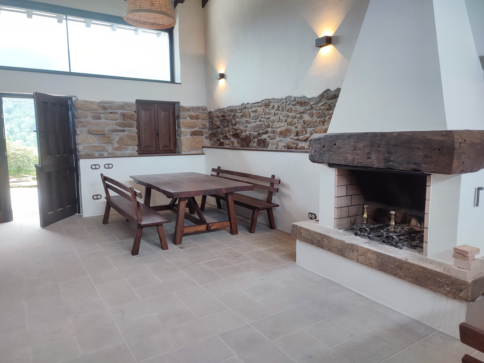 Comedor rústico con mesa, bancos de madera y chimenea de piedra